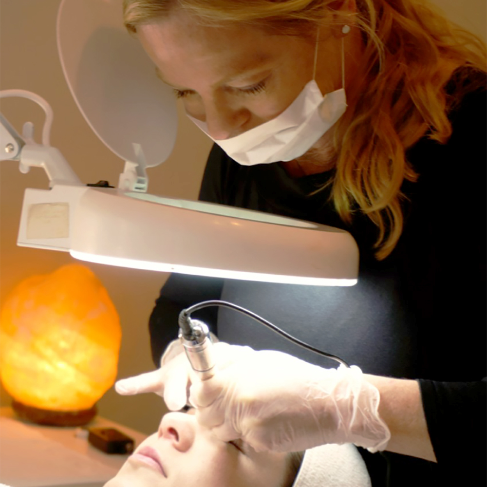 Cathi Wood, experienced cosmetic tattooist, working on a client's eyebrows using a magnifying lamp at Janine's Skin & Laser Clinic.