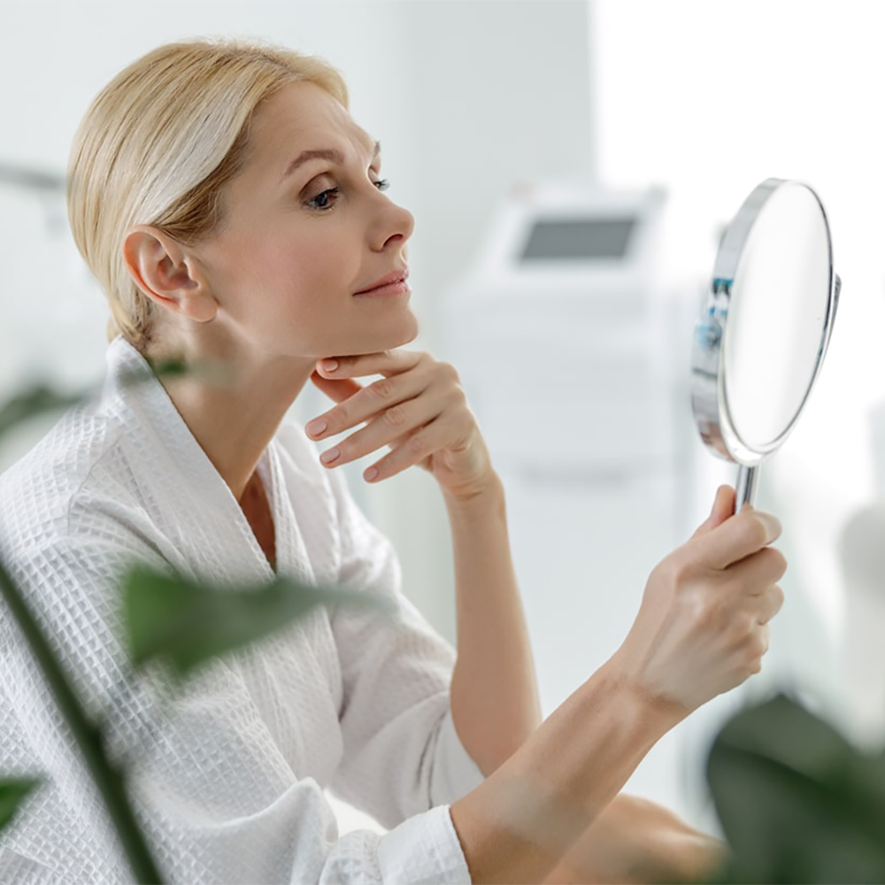 Person smiling at their radiant skin reflection in the mirror after Clear + Brilliant treatment.