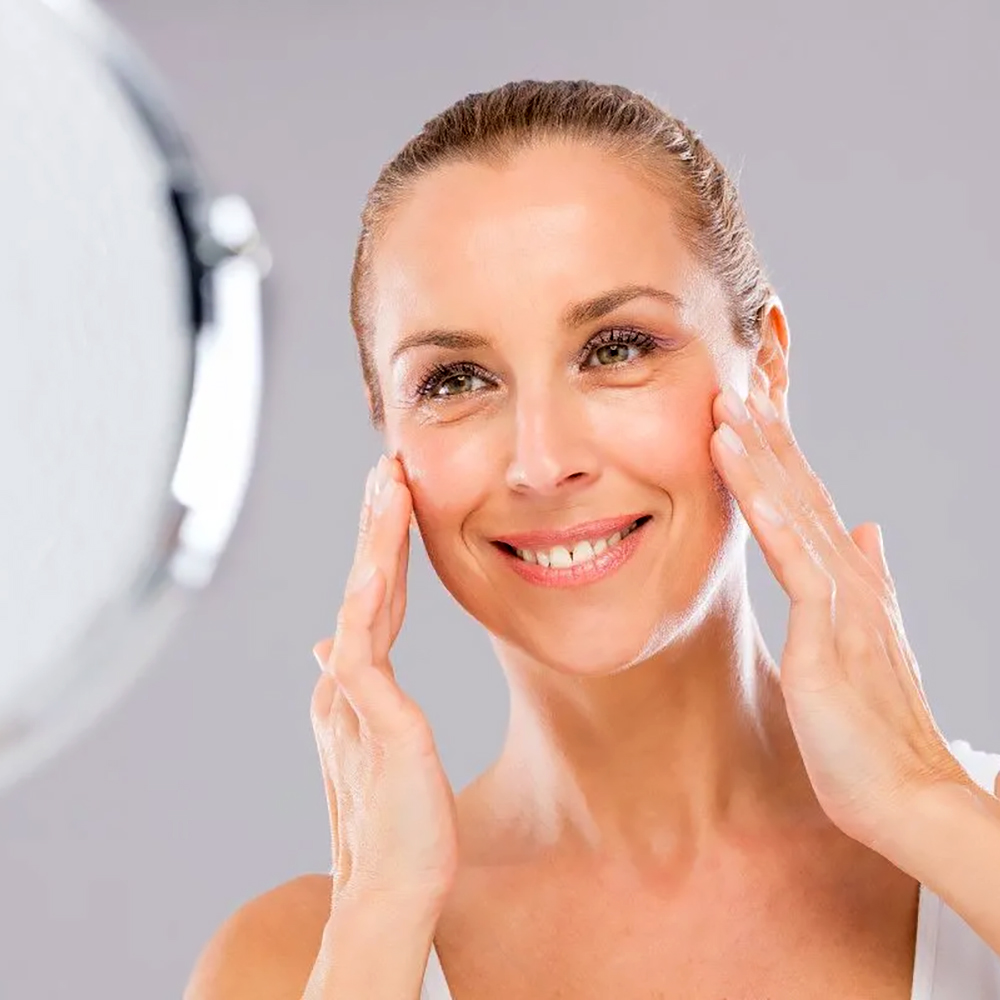 Smiling patient admiring her radiant skin in the mirror after Clear + Brilliant treatment.