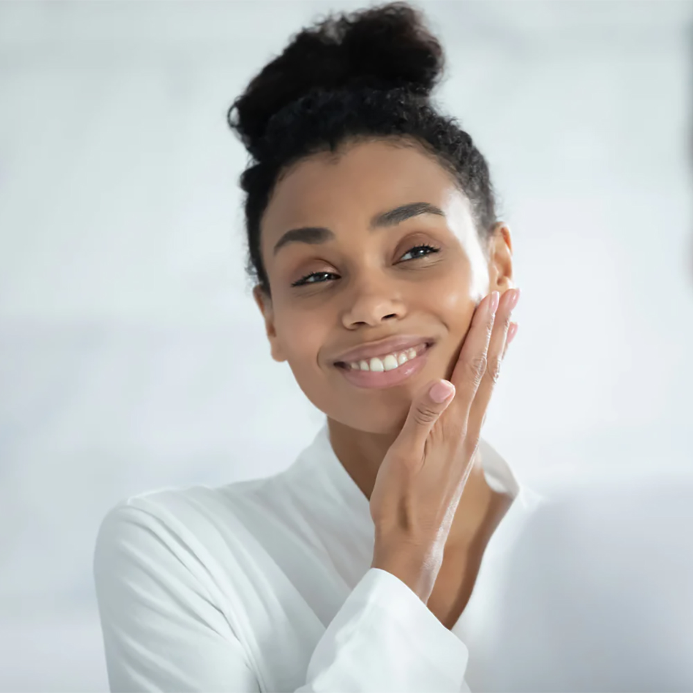 Woman smiling at her reflection in the mirror, satisfied with her skin's rejuvenation post-treatment.